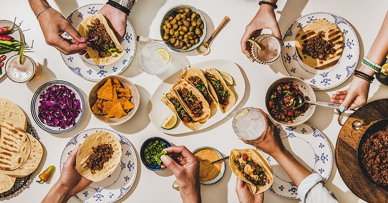 Image showing a spread of ingredients and people preparing their tacos